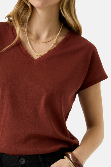 Brick red short-sleeve V-neck T-shirt with ribbed trim, shown on model with layered necklaces and black pants, cropped front view