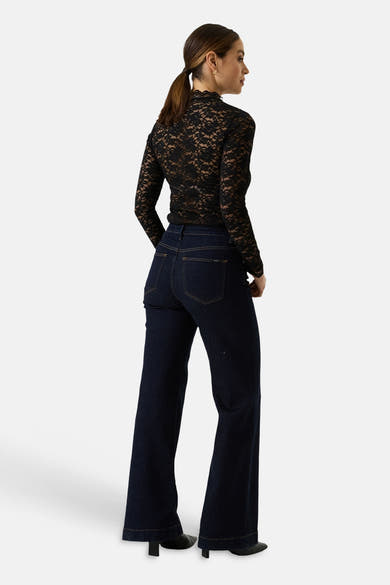 Black long-sleeve lace top with scalloped neckline, back view, paired with dark denim flared jeans and black heels