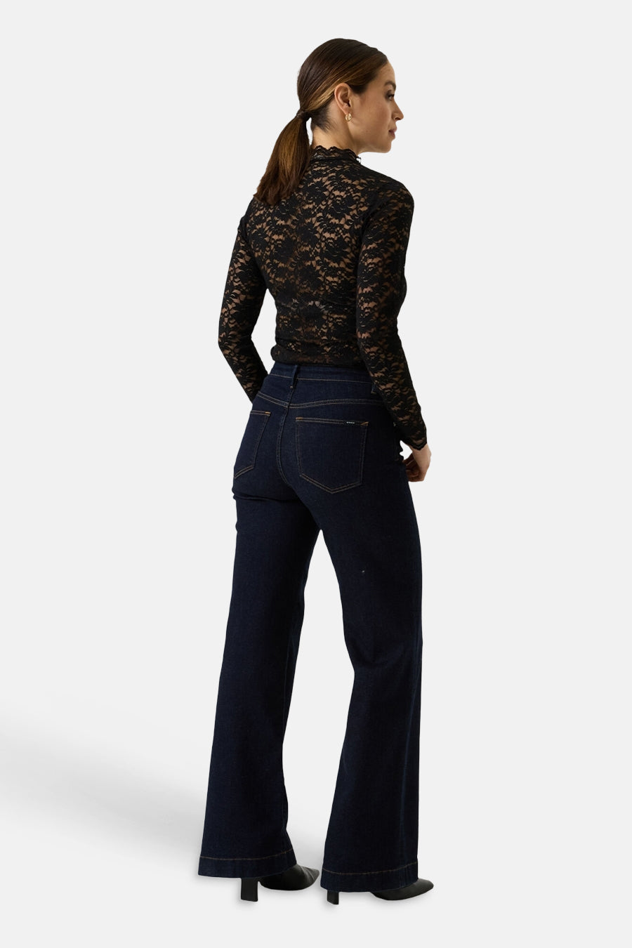 Black long-sleeve lace top with scalloped neckline, back view, paired with dark denim flared jeans and black heels