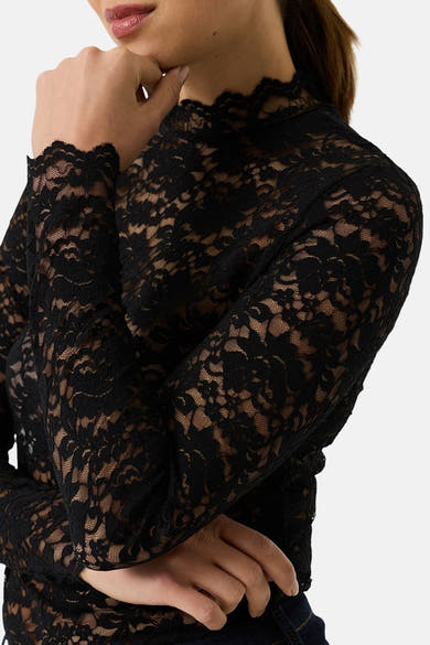 Black long-sleeve lace top with floral pattern and high neckline, side view, model wearing dark jeans