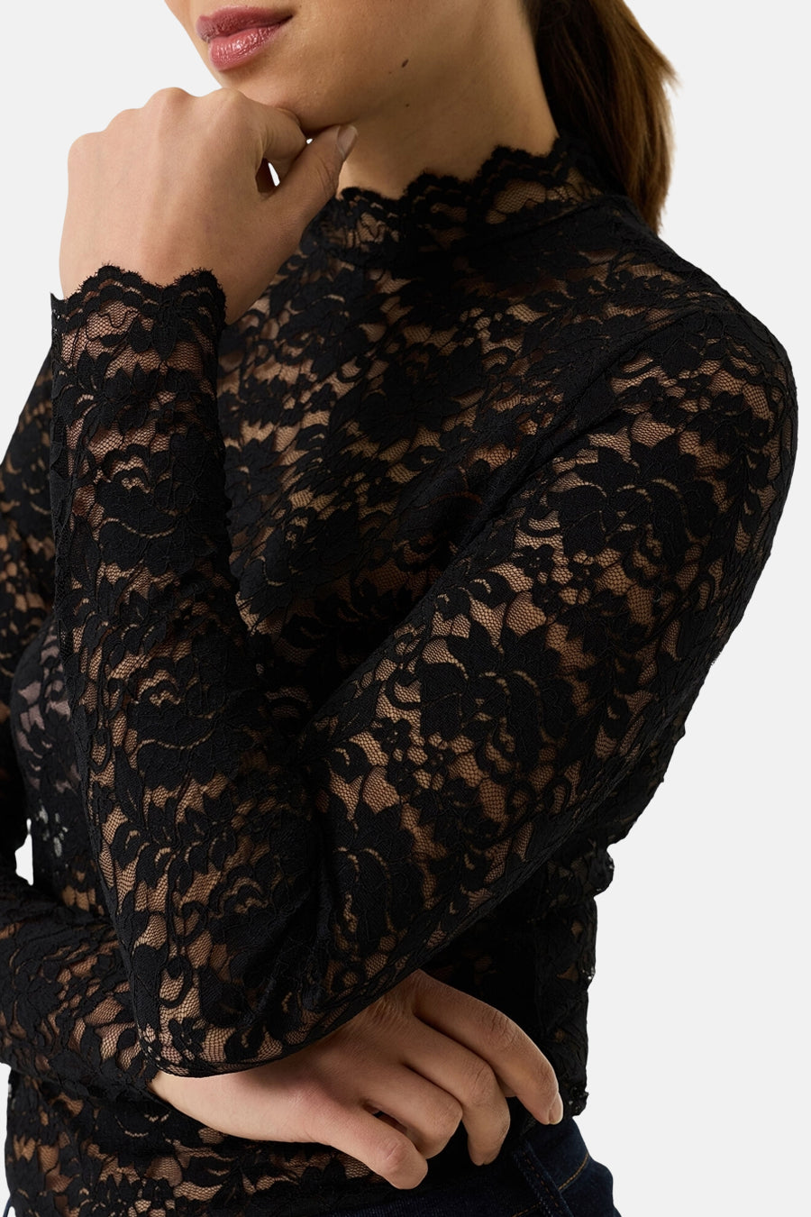 Black long-sleeve lace top with floral pattern and high neckline, side view, model wearing dark jeans