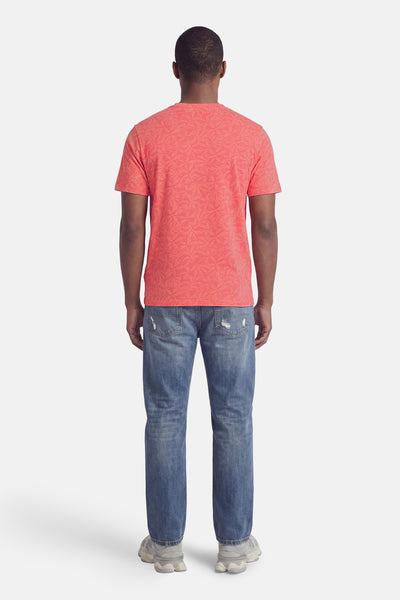 Coral short-sleeve t-shirt with floral pattern, back view, worn with blue jeans and light gray sneakers