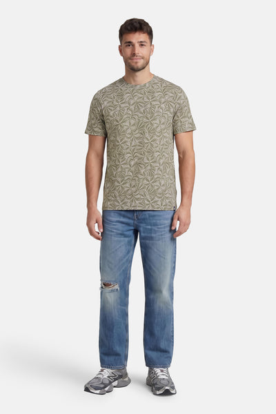 Multicolored short-sleeve t-shirt with leaf pattern, worn by model in full-length lifestyle view with distressed jeans and sneakers.