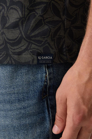 Blauw T-shirt met bladerenpatroon, van Garcia, gedragen met een blauwe spijkerbroek en een zichtbare hand.