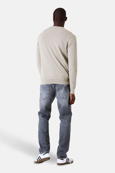 Kaki V-hals trui van GARCIA, gedragen met een lichtgrijze jeans en witte sneakers met strepen.