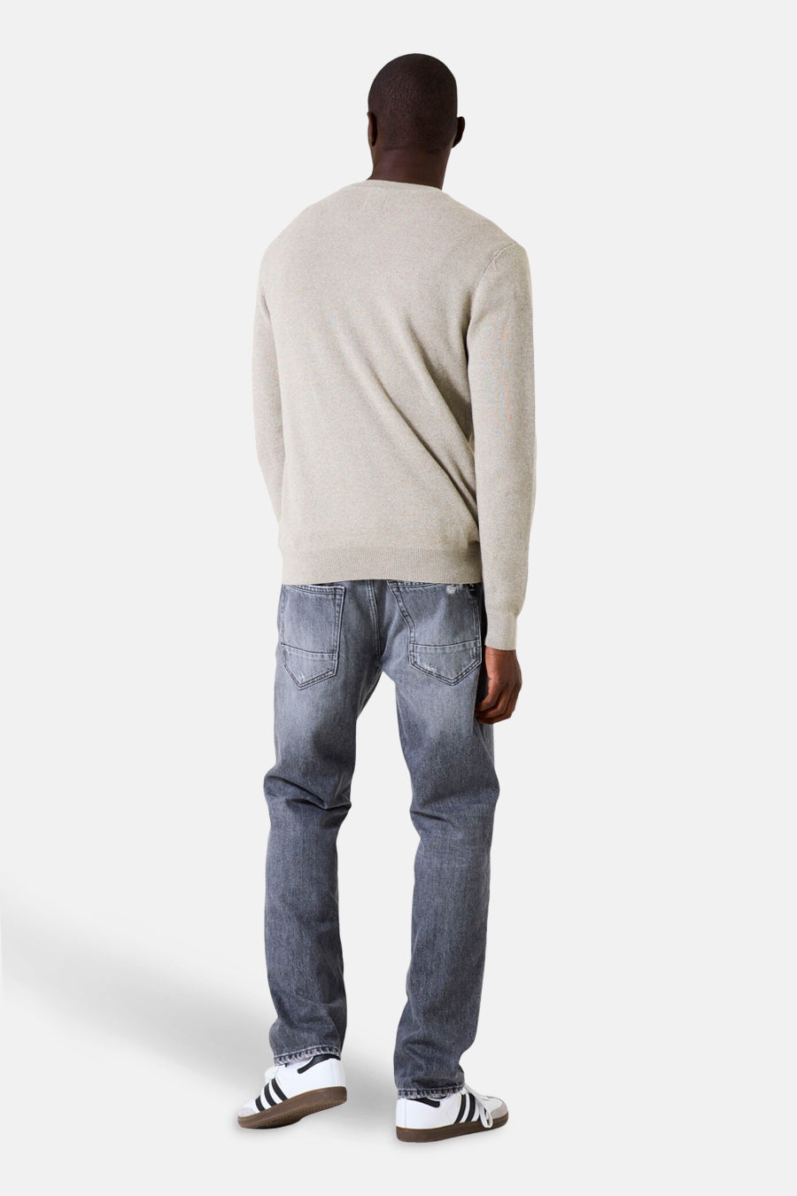 Kaki V-hals trui van GARCIA, gedragen met een lichtgrijze jeans en witte sneakers met strepen.