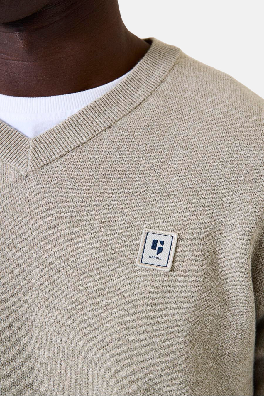 Kaki V-hals trui van GARCIA, met een discreet vierkant logo-patch en een zichtbaar wit T-shirt bij de hals.