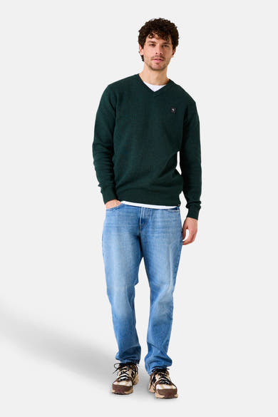 Groene V-hals trui van GARCIA gedragen over een wit T-shirt en een lichtblauwe jeans met bruine sneakers.
