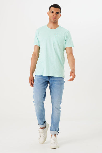 T-shirt turquoise à manches courtes de GARCIA, avec poche poitrine visible, porté avec un jean et des baskets blanches.
