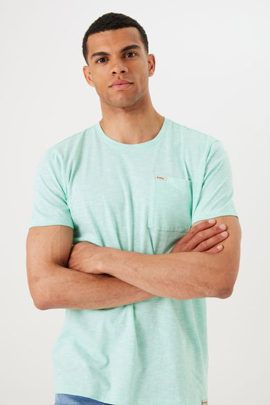 T-shirt à manches courtes turquoise de GARCIA, avec poche poitrine et un homme les bras croisés.