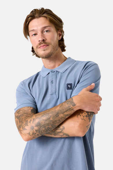 Polo bleu à manches courtes de GARCIA, porté par un homme avec des tatouages sur les bras.

