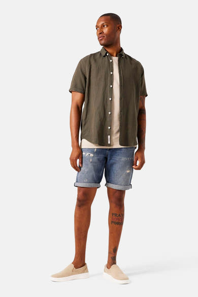 Kaki overhemd met korte mouwen van GARCIA, met witte knopen, gedragen met een zandkleurig T-shirt en een verbleekte spijkerbroek.
