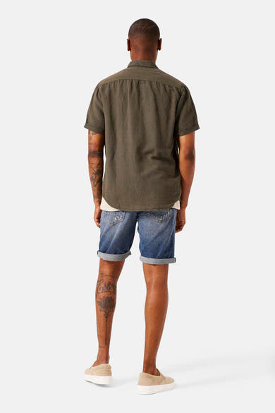 Kaki overhemd met korte mouwen van GARCIA, van achteren gezien, gedragen met een wit T-shirt en een spijkerbroekshort.