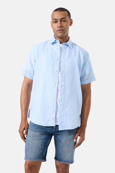Chemise bleu clair à manches courtes de GARCIA, portée ouverte sur un t-shirt blanc et un short en jean.