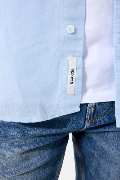 Chemise bleue à manches courtes de GARCIA, avec étiquette de la marque et boutonnage apparent, portée sur un t-shirt blanc et un jean.