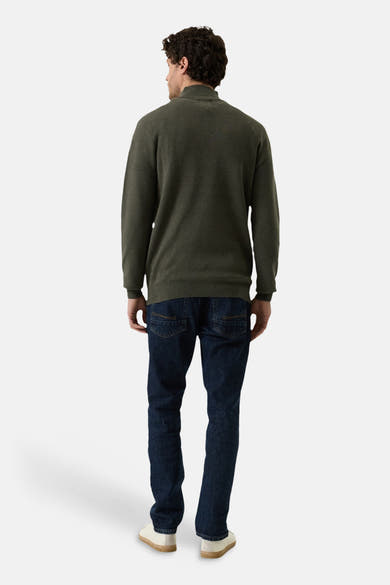 Olive green turtleneck sweater from back view, ribbed cuffs and hem, worn with dark denim jeans and white sneakers