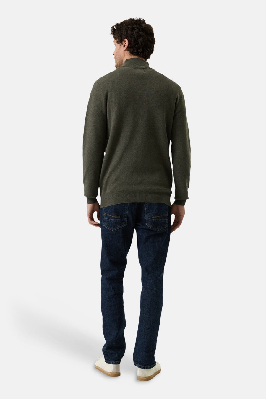 Olive green turtleneck sweater from back view, ribbed cuffs and hem, worn with dark denim jeans and white sneakers