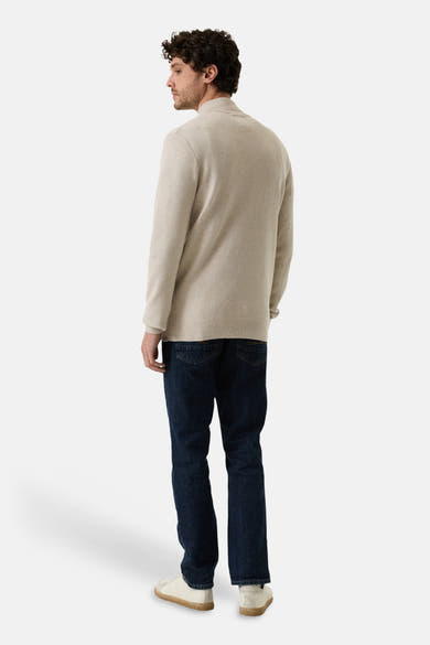 Beige ribbed knit turtleneck sweater from side view, worn with dark denim jeans and white sneakers