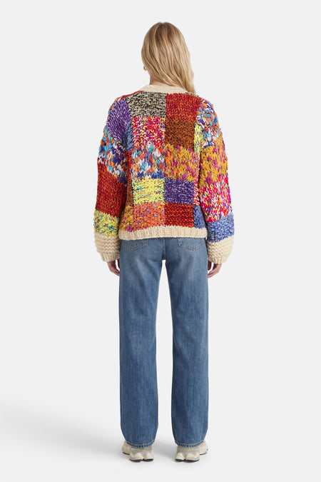 Cardigan multicolore d'ADORE, motif patchwork tricoté, porté avec un jean bleu ample.
