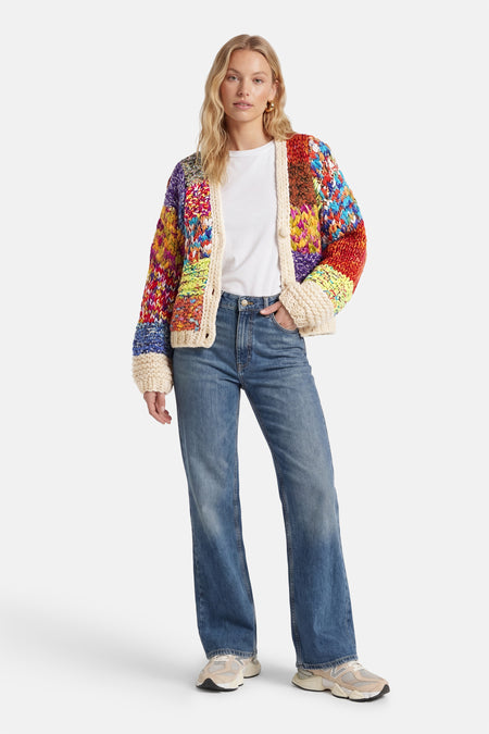 Cardigan multicolore d'ADORE avec une texture tricotée à motifs et porté sur un t-shirt blanc avec un jean ample et des baskets.
